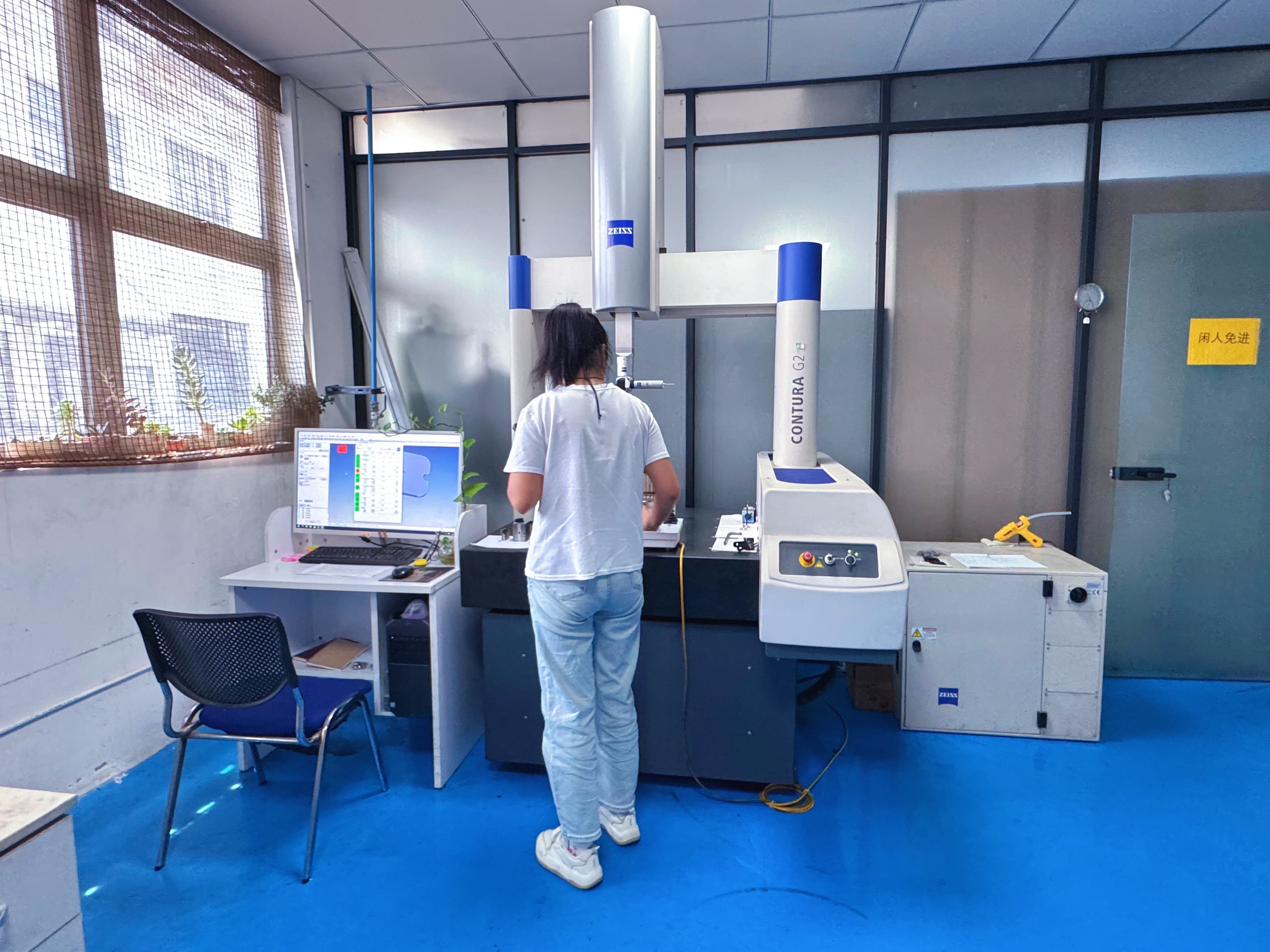 Inspector loading a part on a ZEISS CONTURA G2 coordinate measuring machine with results on the monitor